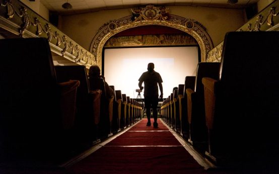 Interior de una sala de cine histórica con butacas tradicionales y proyector antiguo